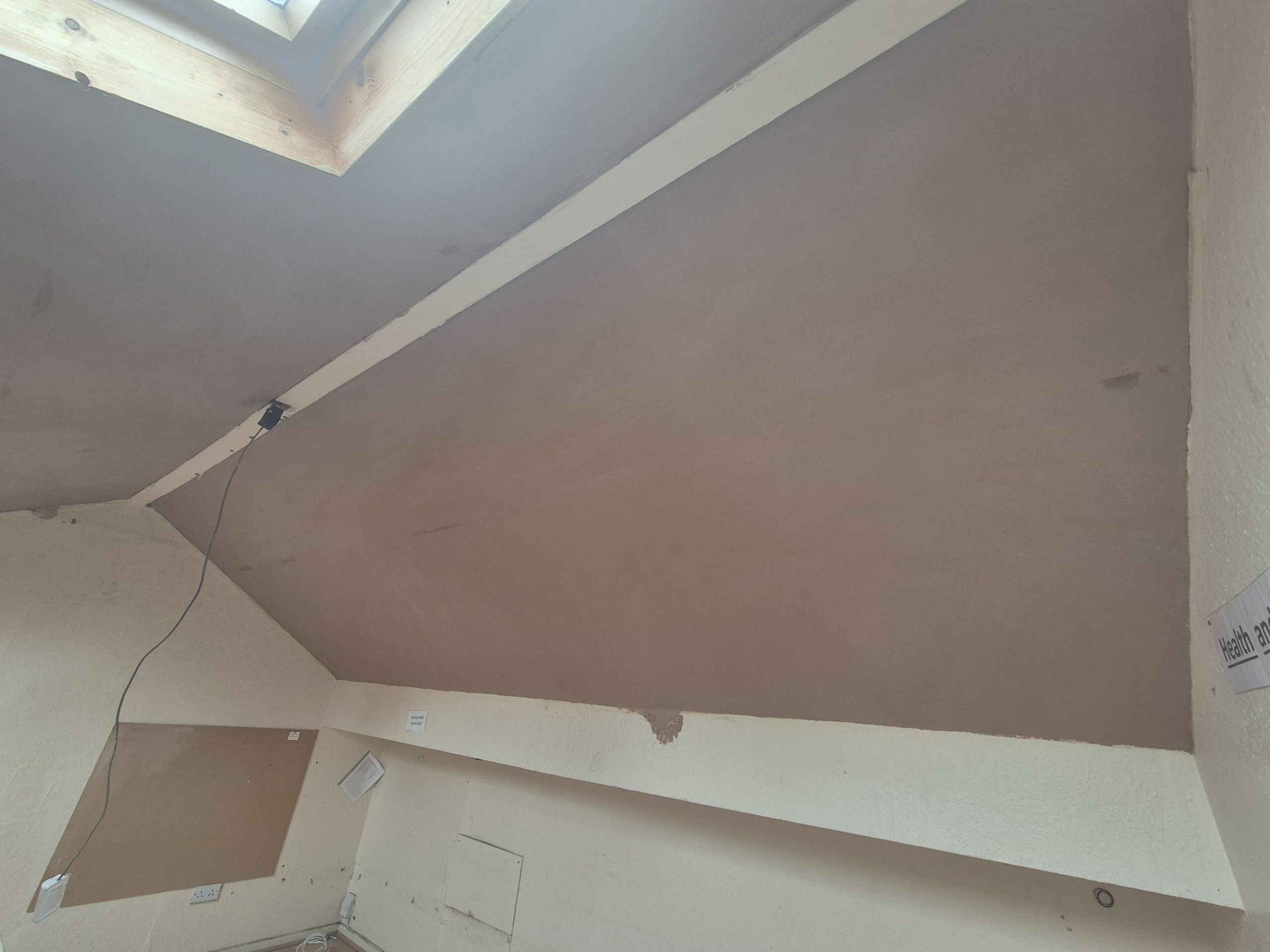 Fresh plaster applied to a vaulted ceiling around a roof window